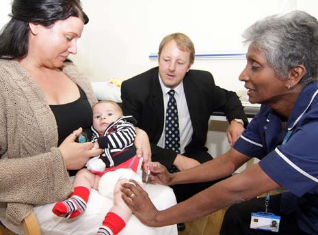 Baby Giro, 12 weeks old, receiving his second set of vaccines from practice nurse Anna Jenkinson, with his mum, Mrs Petrillo and Toby Perkins MP